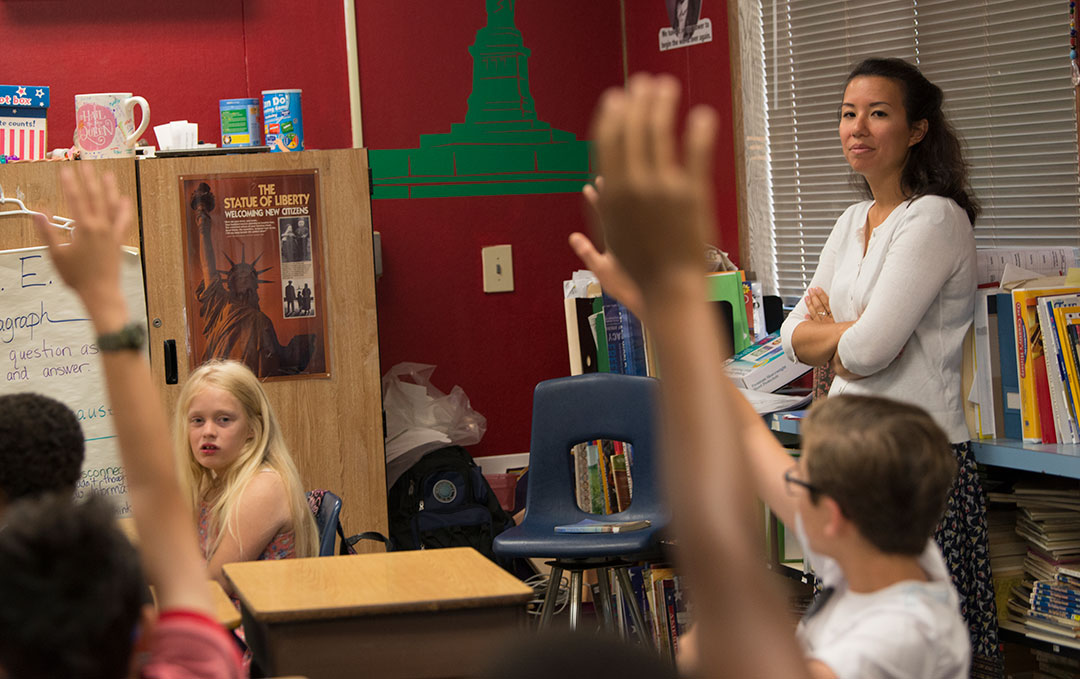 Teacher standing in classroom, raised hands in foreground