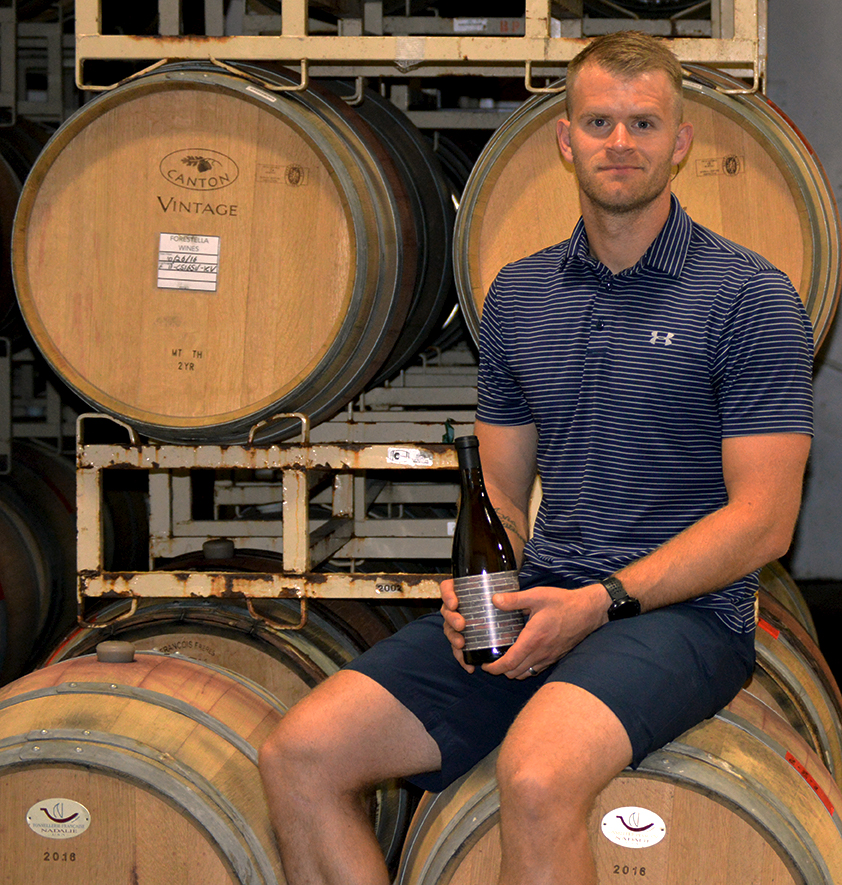 Matt Iaconis posing with a bottle of wine in a barrel room