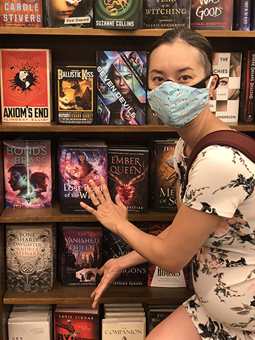 Andrea Stewart wears a face mask stands next to her books at a bookstore.