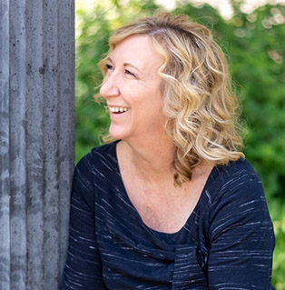 Blonde, curly haired and middle-aged woman smiling and looking up to the left