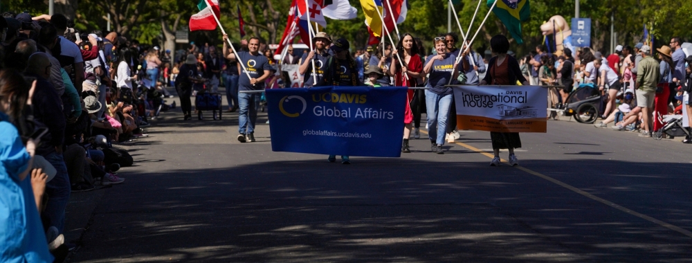 Group of Global Affairs staff and community members holding various countries' flags while marching in a parade.