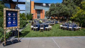 Round tables with blue linens and tablecloths, as well as gold chiavari chairs set up at the Good Life Garden for the Alumni Awards.