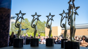 Six golden awards are displayed in a semi-circle on a table facing the audience.