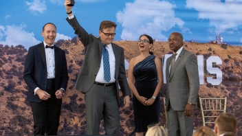 John M. Wasson ’84 lifts his golden award in the air and is flanked by former Board President Charles Melton ’08, AVC Dana Allen, and Chancellor Gary May on stage.