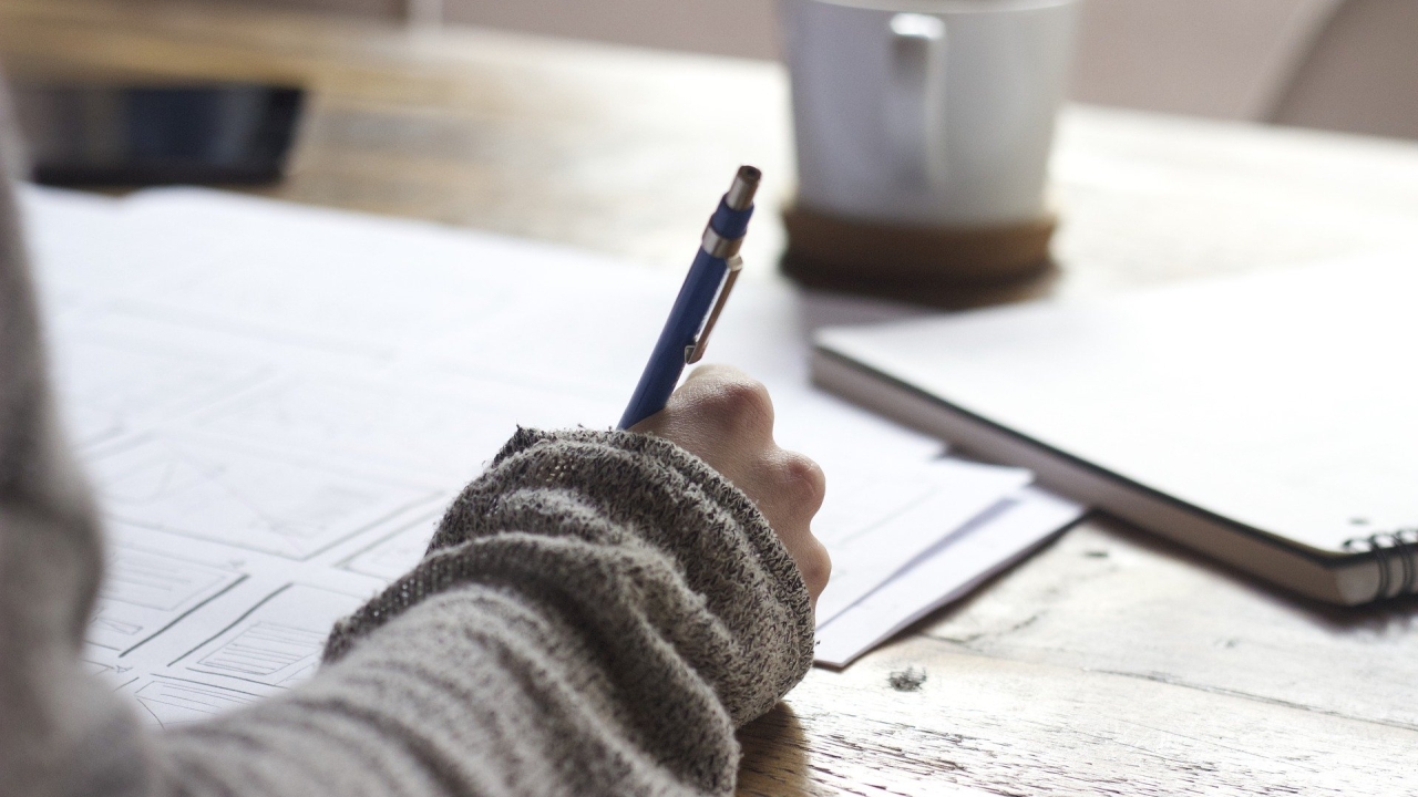 Hand holding a pen writing on paper on a desk with coffee nearby