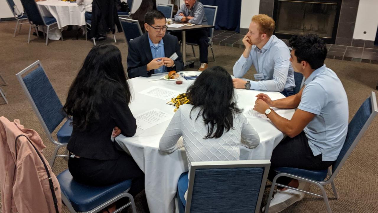 Picture of students and an alumni talking at a table.