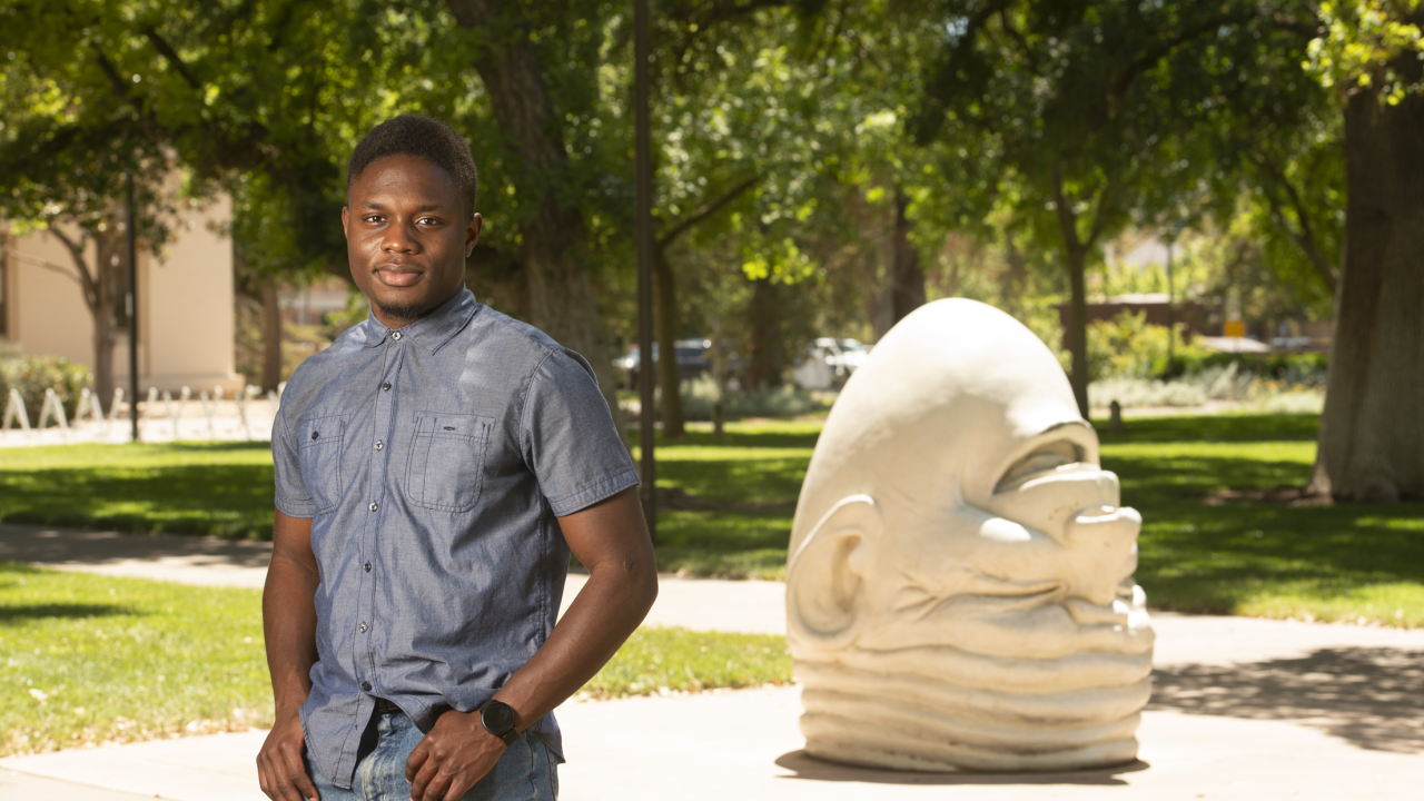 Chidubem Nnaji standing on campus with Egghead sculpture in the background