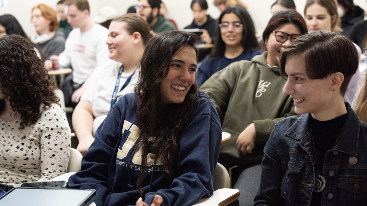 photo of a classroom at UC Davis. Students are seated in a lecture style room and the photo is focused on two students facing each other and conversing