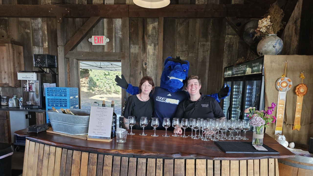 Gunrock poses with two bartenders behind the bar of a rustic winery.