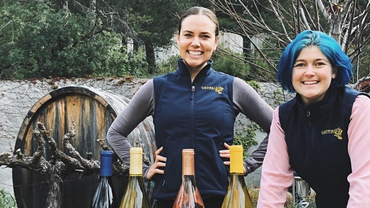 two people standing by wine bottles with trees in the background