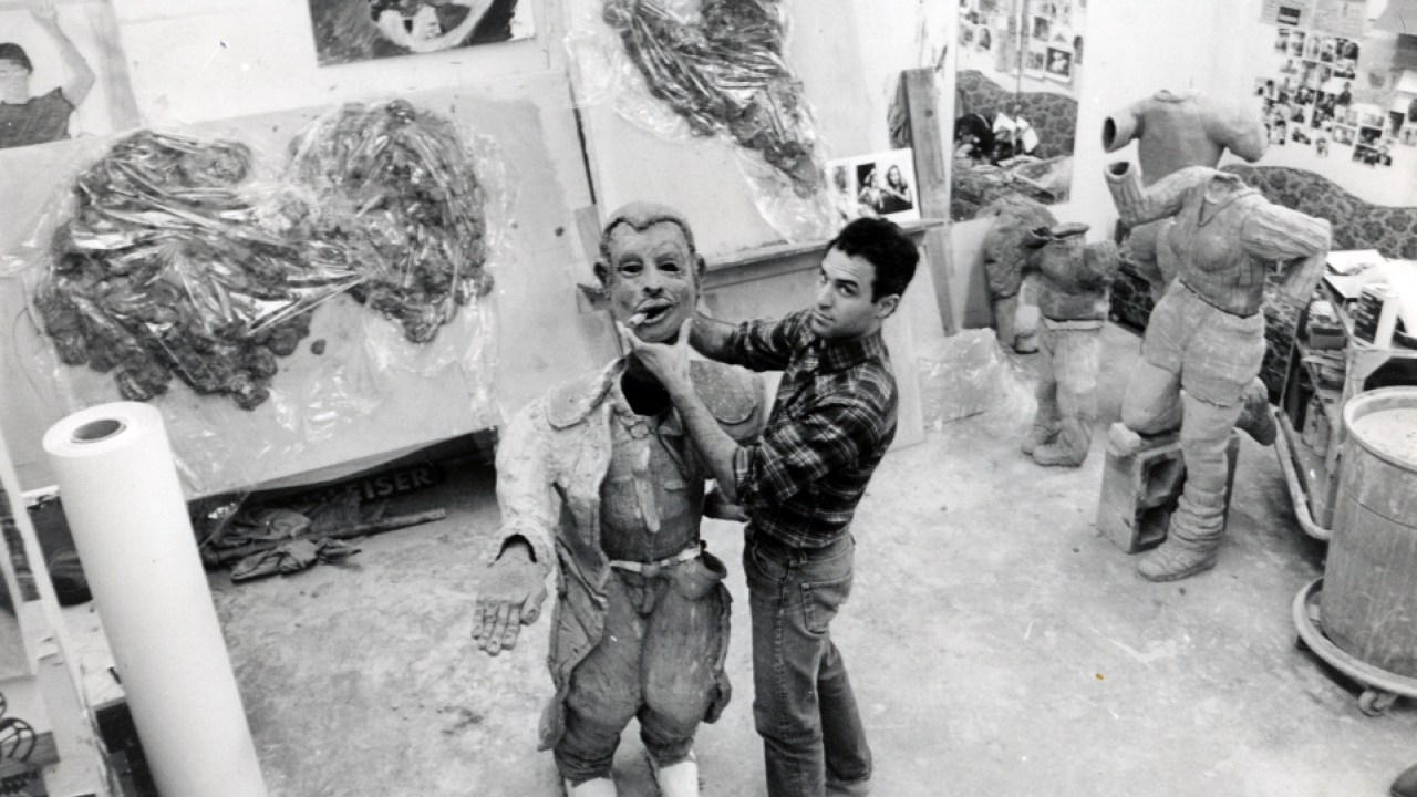 Black and white photo of Natsoulas in an art studio holding the head of his full-body sculpture.