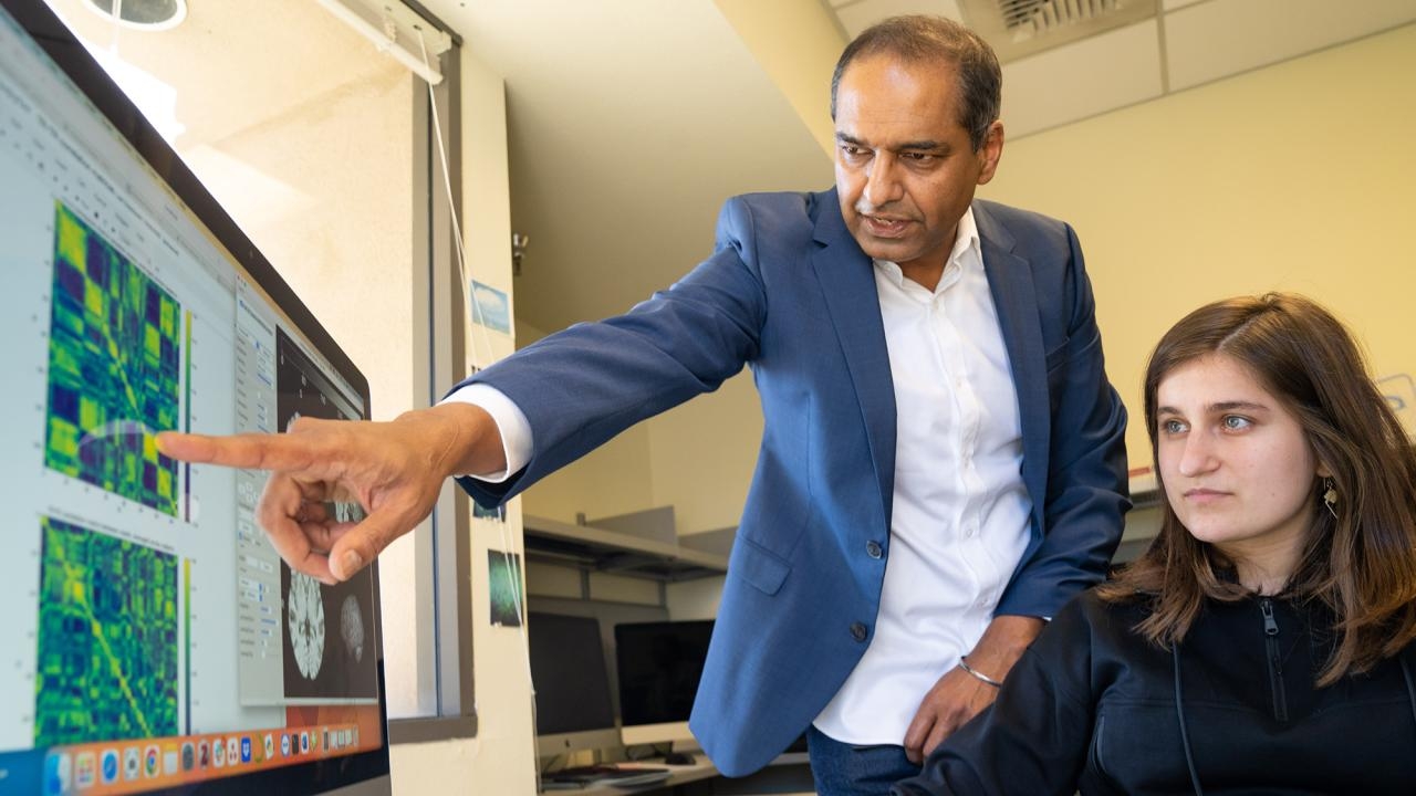 A professor points at a computer screen next to a student