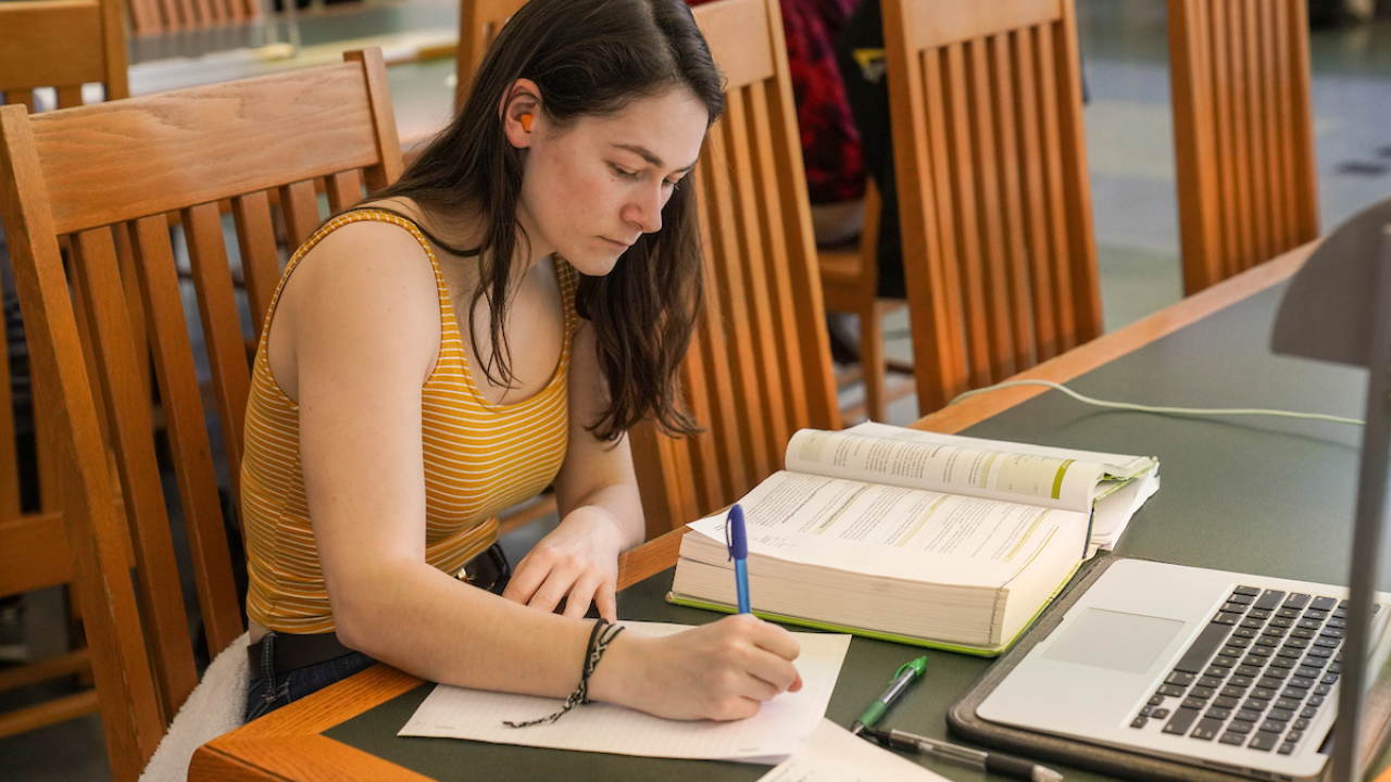 girl sitting in Shields Library writing on a notebook