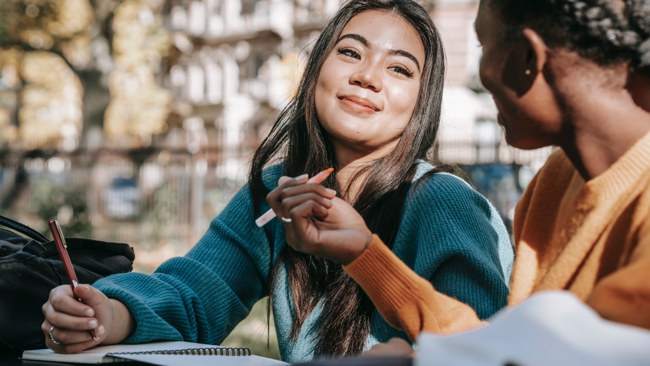 Image of two students taking notes and talking to each other