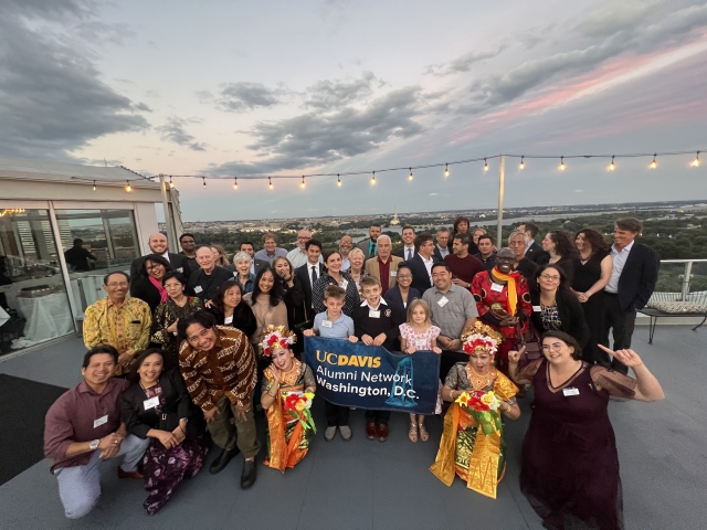 A group of UC Davis community members pose on the rooftop in front of the Potomac River in the horizon.