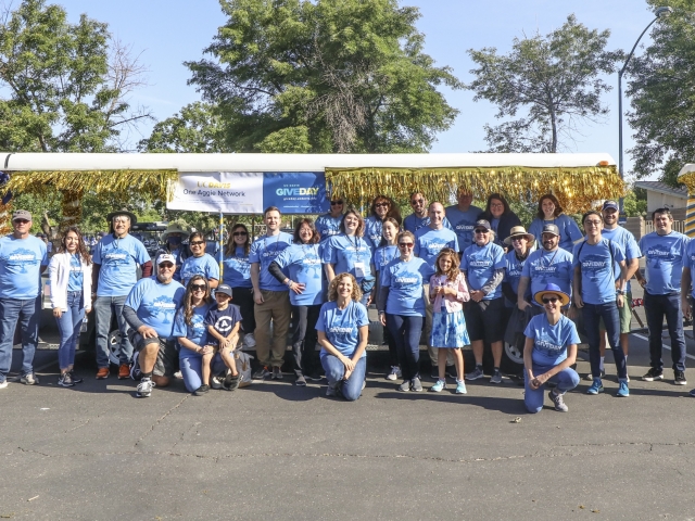 A group of volunteers wearing matching blue &#34;Give Day&#34; shirts pose for a photo in front of the tram as part of the Picnic Day parade.