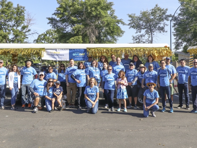 A group of volunteers wearing matching blue &#34;Give Day&#34; shirts pose for a photo in front of the tram as part of the Picnic Day parade.