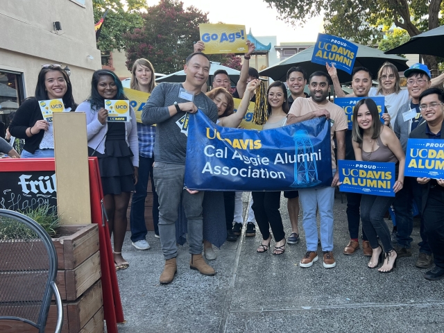 Group photo of alumni and volunteers posing with UC Davis alumni signs. Two people hold the Cal Aggie Alumni Association vinyl banner.