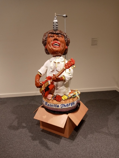 Large ceramic sculpture of singer Sister Rosetta Tharpe looking upwards playing guitar and singing into a microphone