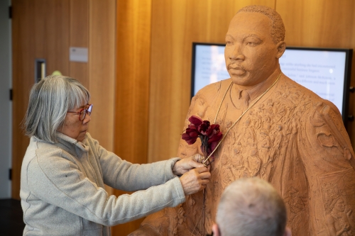 Alum adorns a Martin Luther King Jr. statue with a red flower.