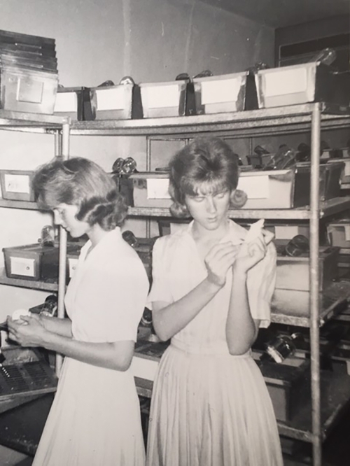 Black and white photo of twin sisters holding mice in lab with shelves and boxes in background.