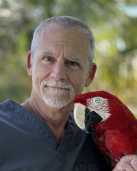 Dr. Doug Mader poses with a red macaw outdoors.