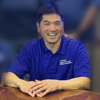 Thomas Yih wearing a blue polo shirt leaning against a desk.