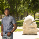 Chidubem Nnaji standing on campus with Egghead sculpture in the background