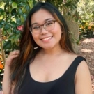Arianna Dela Rosa poses in glasses and a black sleeveless top in front of green foliage.