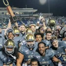 UC Davis football players wearing grey uniforms holding up the Golden Horseshoe Trophy in celebration