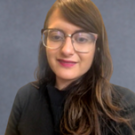 Headshot of Star Ghanaat wearing glasses and a black top in front of a dark grey background.