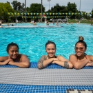 Three women are smiling with their arms on the edge of the UC Davis Rec Pool