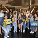 Group of people facing the camera holding blue & gold pompoms and cheer cards