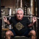 Rudy Kadlub squatting and holding a barbell at his shoulder in a gym.