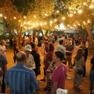 image of a group of people mingling under lights outside during the evening