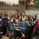 15 people facing the camera, with the 3 in front holding a banner reading, "UC Davis Cal Aggie Alumni Assocation"