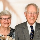 Cathy and Bob Kerr wearing business casual attire in front of a blurry background with pillars.