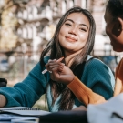 Image of two students taking notes and talking to each other