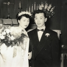 Black and white photo featuring two people in wedding attire with candles and cross behind them.