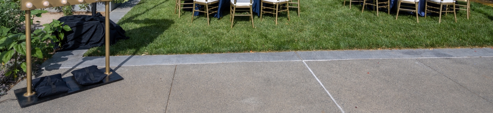 Round tables with blue linens and tablecloths, as well as gold chiavari chairs set up at the Good Life Garden for the Alumni Awards.