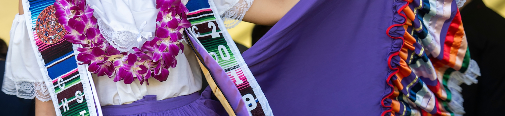 Graduation outfit of a Chicanx Studies major: white shirt with lace, long purple skirt with pattern and ruffles at the end, and a lei.