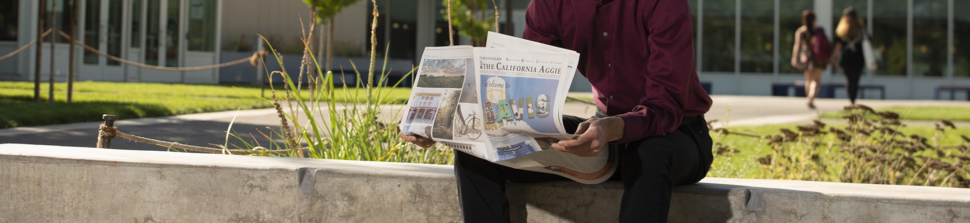 Person in formal attire sitting outside at the Memorial Union reading a copy of the California Aggie newspaper.