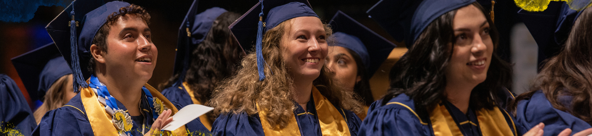 A group of graduates in regalia smiling and facing the same direction.